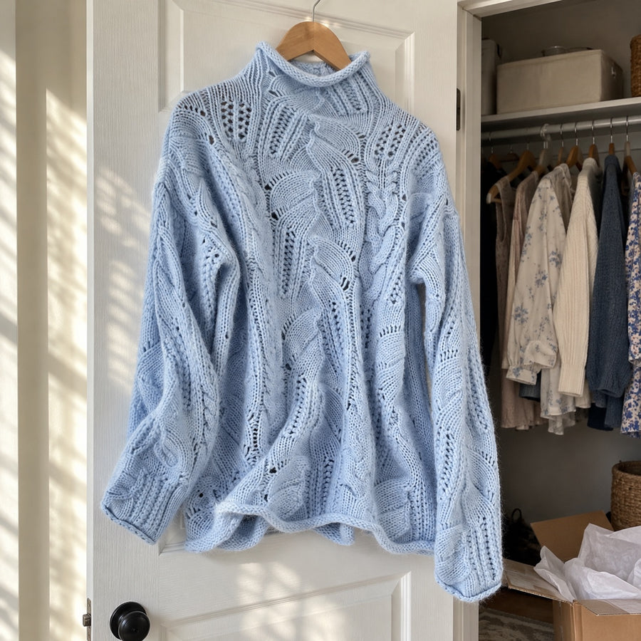 The Aurora sweater on a hanger, showing the cable knit pattern